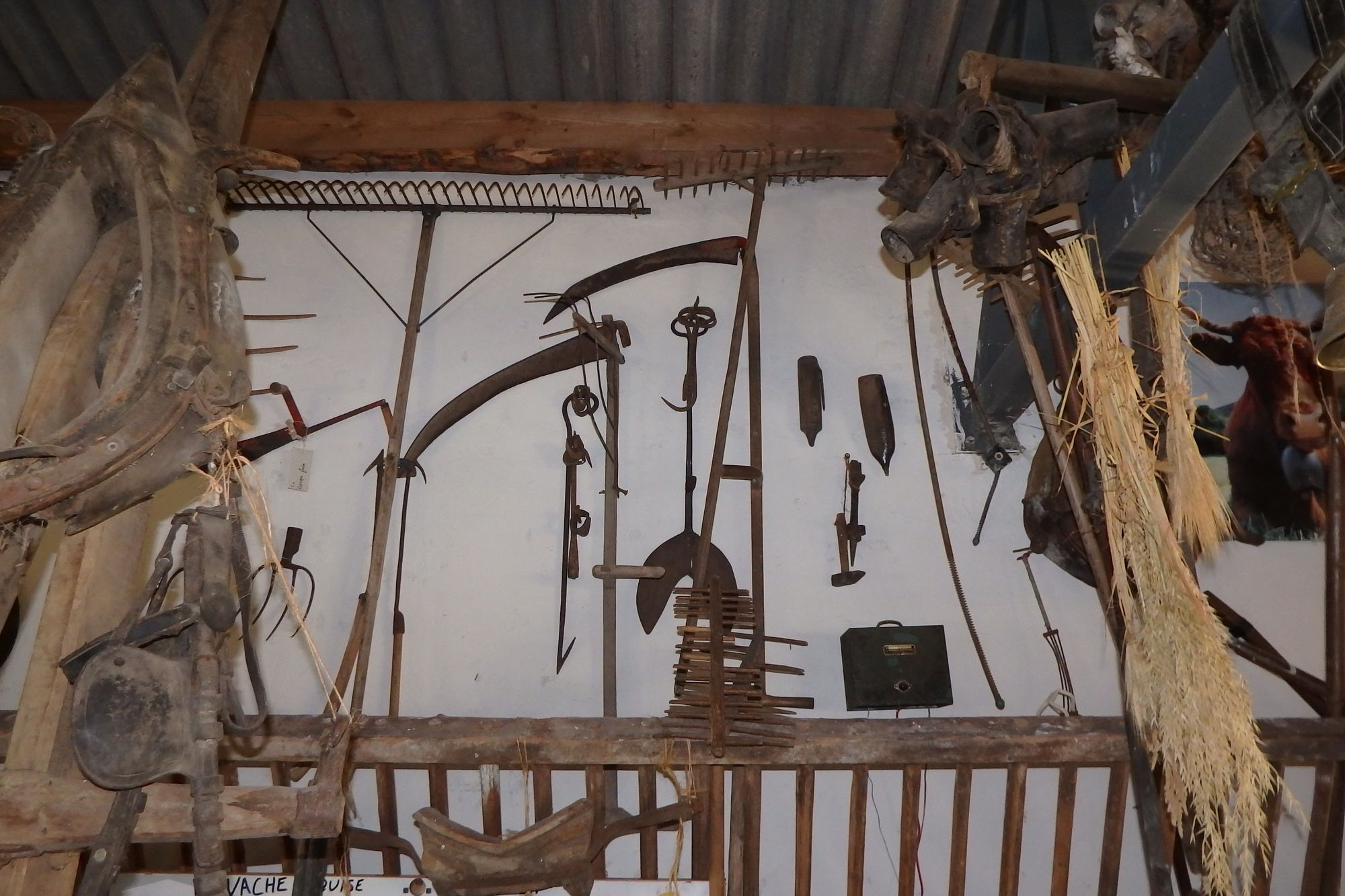 Mur d'outils agricoles anciens : faux, râteau, fourches et colliers d'attelage
